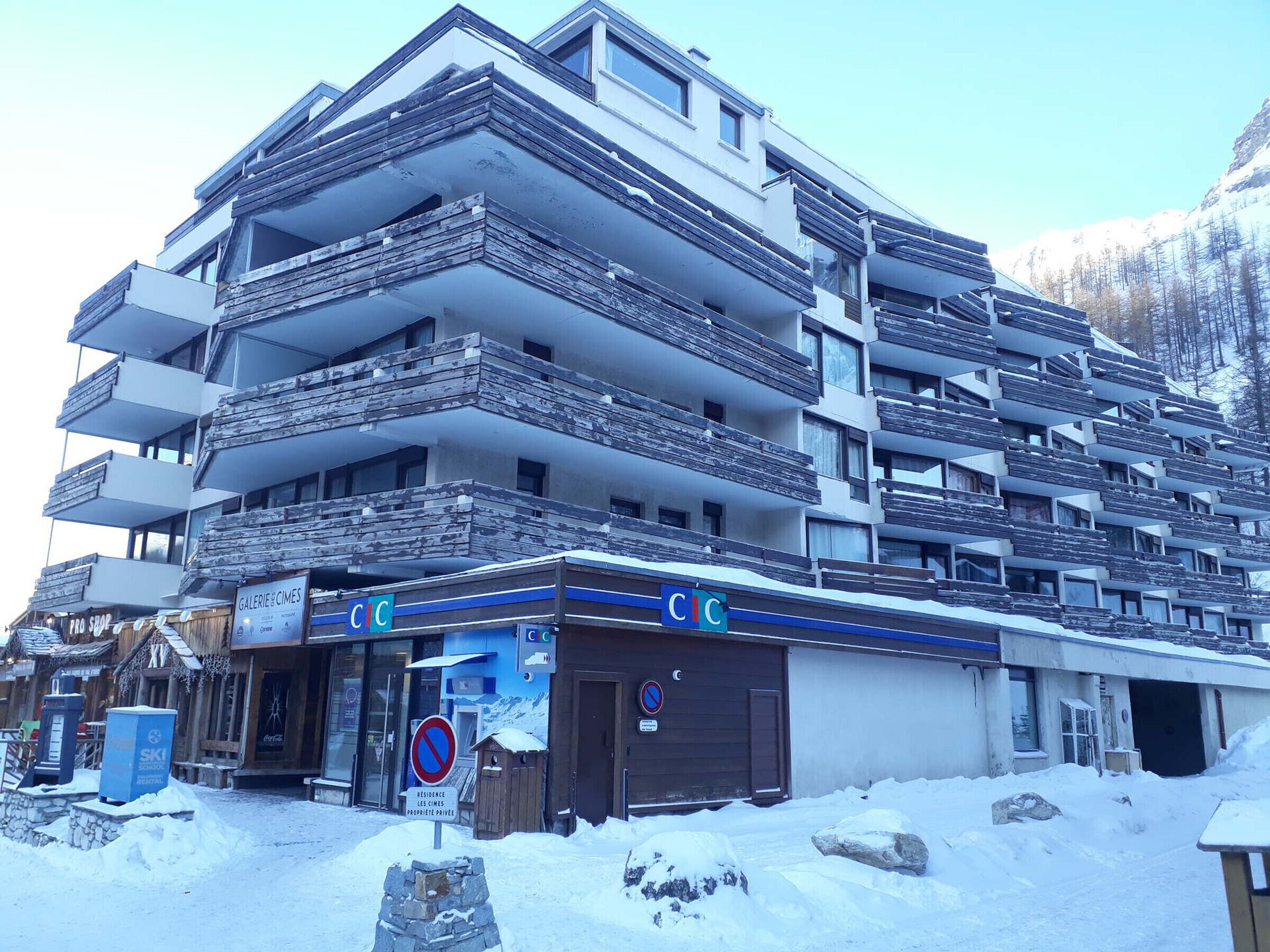 Een meerhoog hotel met balkons, een bord met ski-school en een parkeerverbod-bord.
