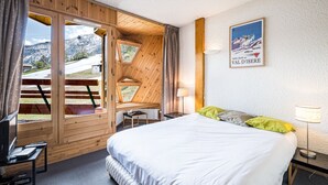 Habitación de hotel con cama, escritorio, silla, televisor y ventana con vista a la montaña.