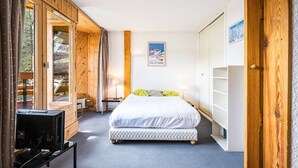 Un dormitorio con cama, escritorio, televisor y ventana con cortinas.
