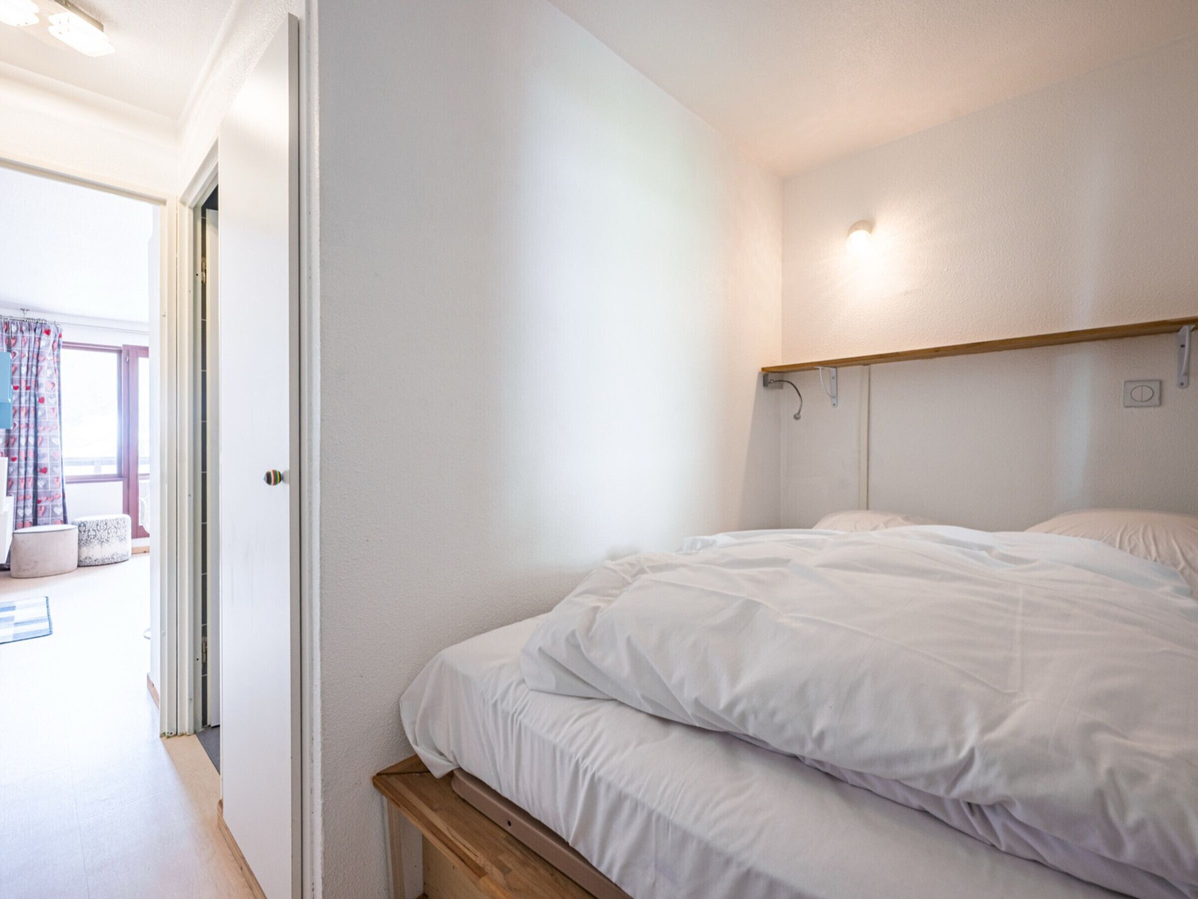 A bedroom with a bed, a door, and a window with curtains.