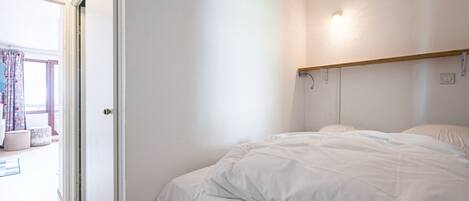 A bedroom with a bed, a door, and a window with curtains.