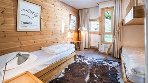 Een kamer met houten wanden, een bed, een bureau, een lamp, een vachttapijt van runderleer en een raam met gordijnen.