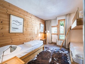 A room with wooden walls, a bed, a desk, a lamp, a cowhide rug, and a window with curtains.