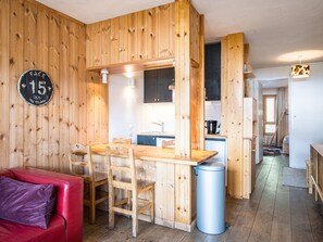 A wooden interior with a kitchen area, a dining table with chairs, a red sofa, and a trash bin.