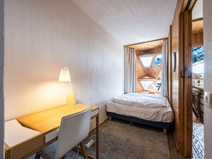 A compact bedroom with a wooden desk, a bed, and a window with curtains.