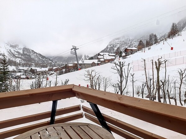 A wooden bench overlooking a snowy mountain village with houses and a ski lift.