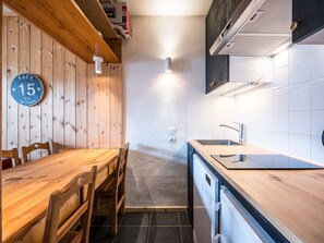 A compact kitchen with wooden walls, a dining table, chairs, a sink, and a stove.