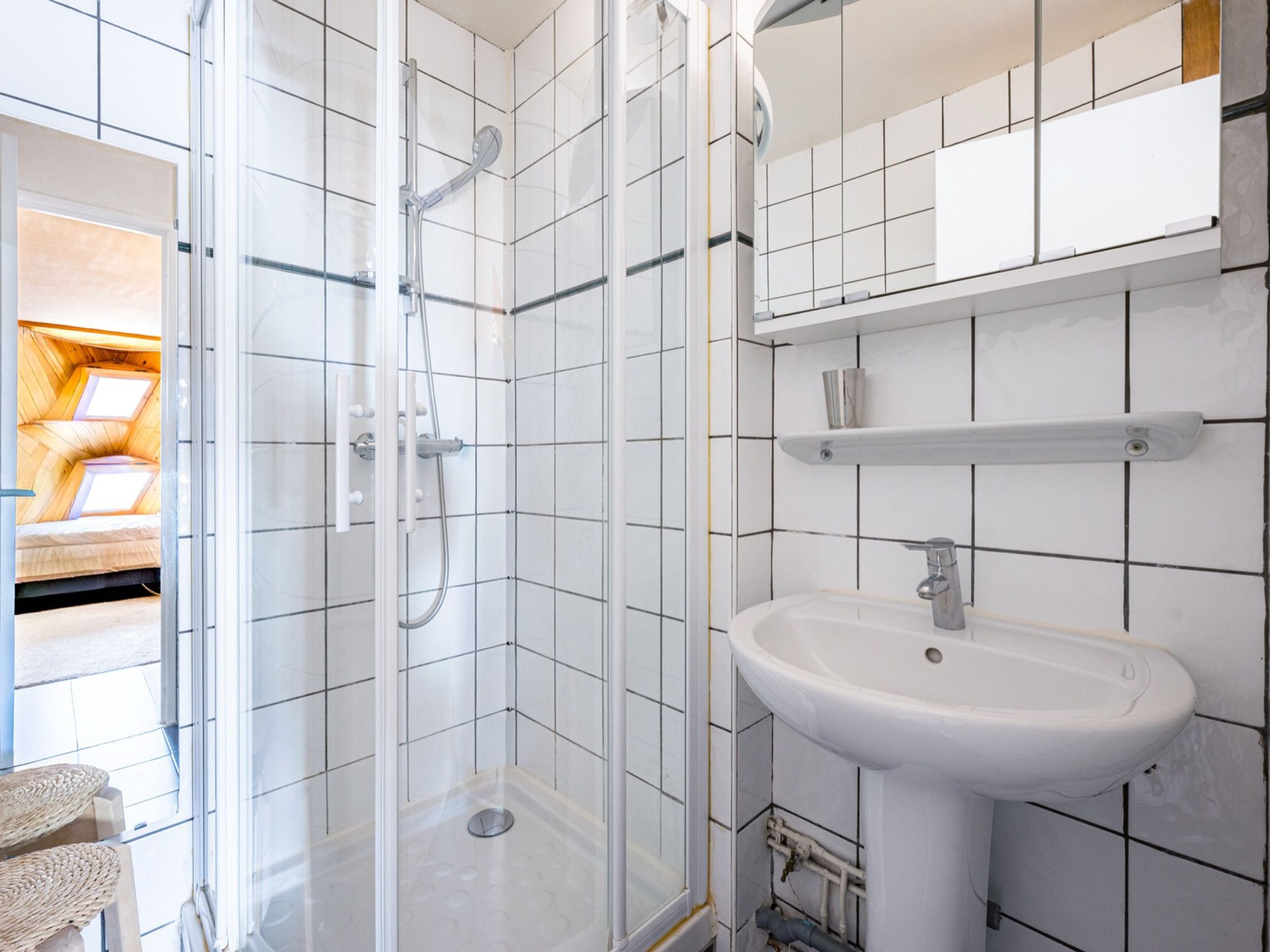 A modern bathroom with a glass-enclosed shower, a white sink, and a tiled wall.