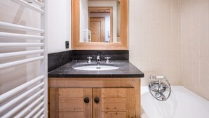 A bathroom with a wooden vanity, a white sink, a mirror, and a bathtub. - Charming Apartment in Chatelard, Val-d'Isère, Direct Access to Slopes, Parking Included (Val-d'Isère)
