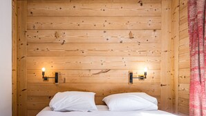 A bedroom with wooden panel walls, two bedside lamps, and a bed with white bedding. - Charming Apartment in Chatelard, Val-d'Isère, Direct Access to Slopes, Parking Included (Val-d'Isère)