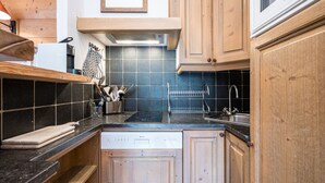 A kitchen with wooden cabinets, a black countertop, a dishwasher, and a hanging rack. - Charming Apartment in Chatelard, Val-d'Isère, Direct Access to Slopes, Parking Included (Val-d'Isère)
