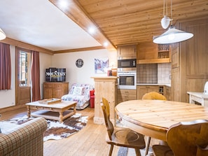 Un salon chaleureux avec un plafond en bois, une télévision, un canapé, une table basse et une table à manger avec des chaises.