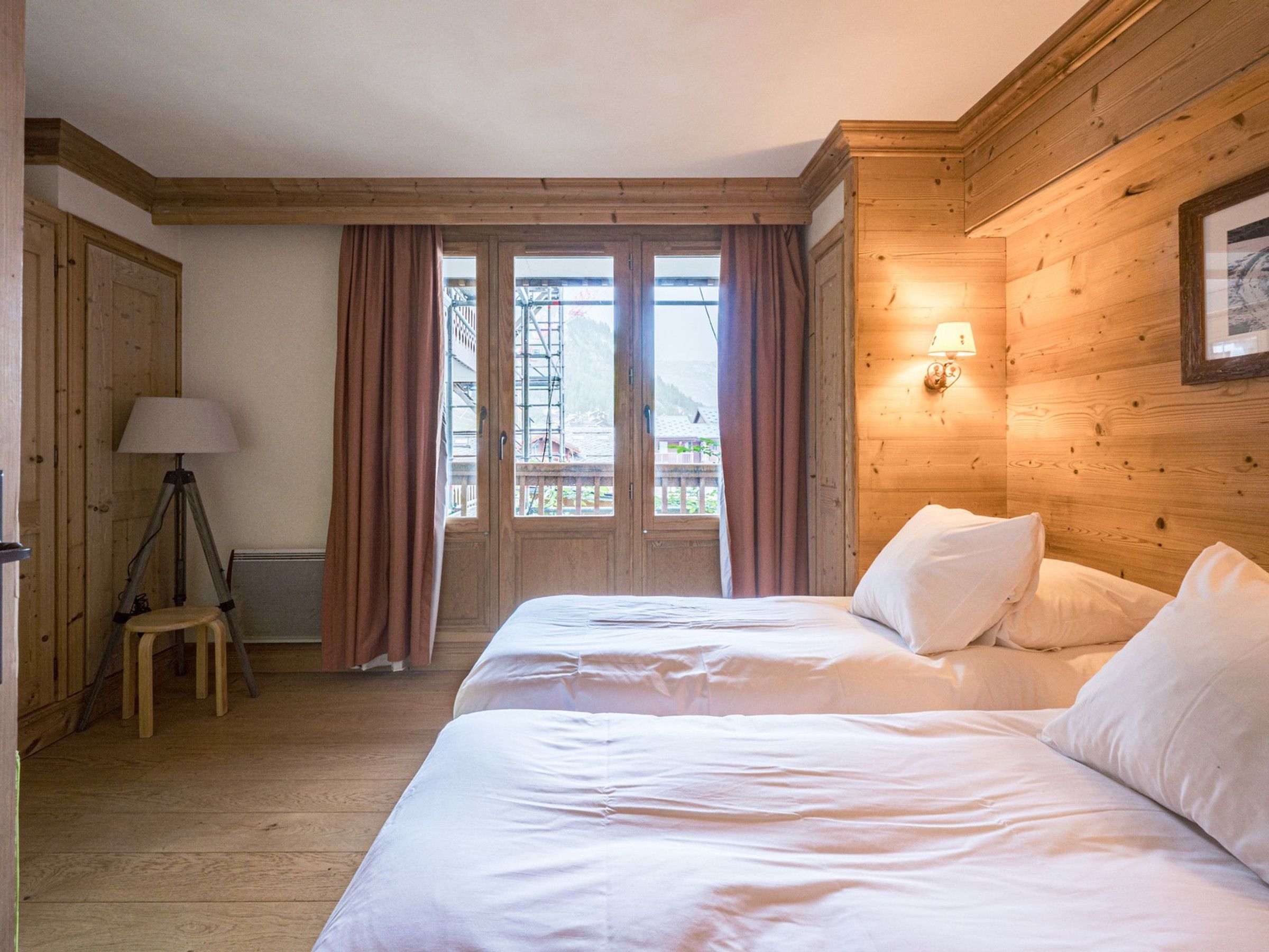A room with a bed, a lamp, a stool, and a window with curtains.