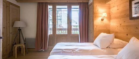 A room with a bed, a lamp, a stool, and a window with curtains.