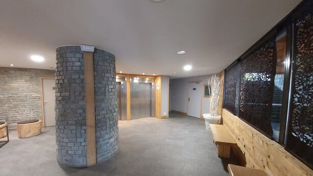 A spacious lobby with a stone pillar, wooden benches, and a large window with decorative glass panels.