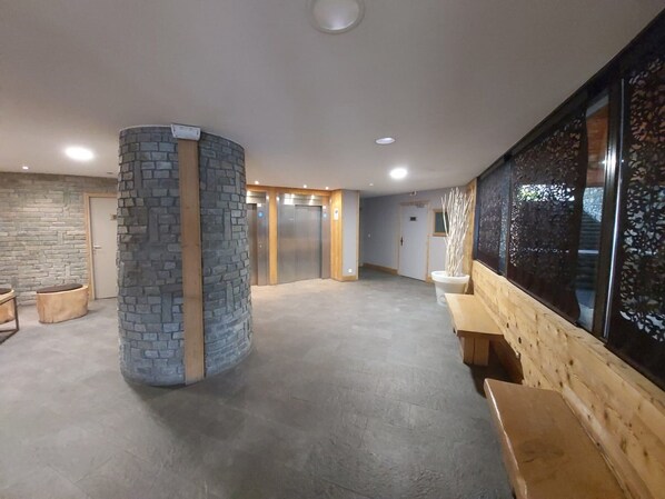 Un hall d’entrée spacieux, agrémenté d’un pilier en pierre, de bancs en bois et d’une grande fenêtre ornée de panneaux de verre décoratifs.