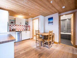 A kitchen with wooden cabinets, a checkered backsplash, a dining table with chairs, and a bathroom with a shower visible through an open door.