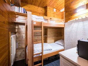 Une chambre avec un lit superposé, un plafond en bois, un radiateur, un bureau et une étagère remplie de livres.