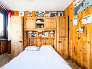 A wooden room with a bed, shelves with books and photos, and a window with curtains. - Bright apartment in Val-d'Isère center for 5 people (Val-d'Isère)