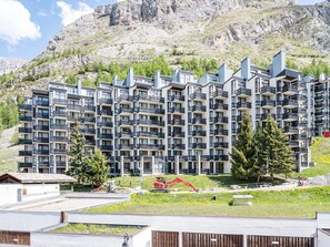 Un hotel a più piani con balconi, uno sfondo montuoso e attrezzature da costruzione a terra.