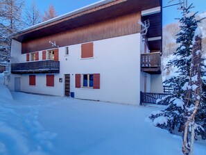 Un edificio de dos pisos con fachada de madera, balcones y suelo cubierto de nieve.
