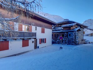 A snow-covered building with a balcony, a no parking sign, and a mountain in the background.