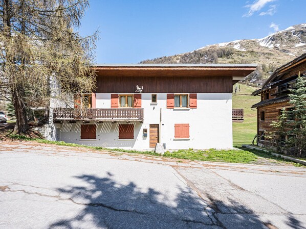 Ein zweistöckiges Gebäude mit Balkon, Holztür und einem kleinen Garten.