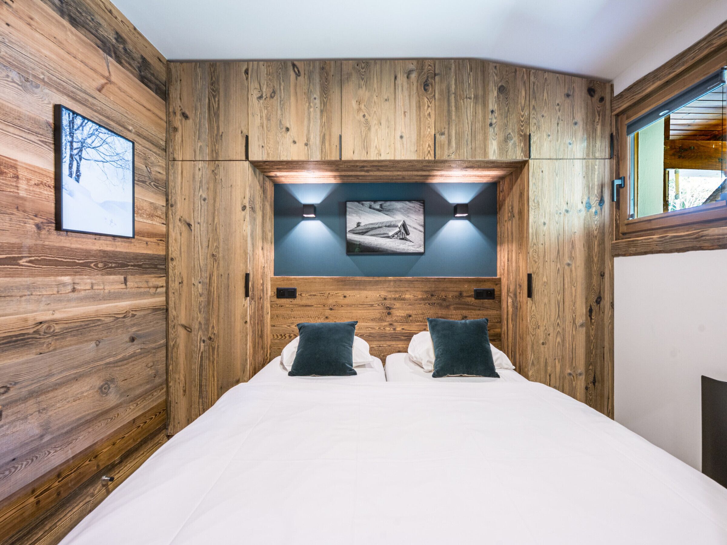 Une chambre avec un panneau mural en bois, un lit avec une literie blanche, deux oreillers et un luminaire fixé au mur.