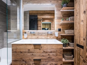 Ein modernes Badezimmer mit einem Holzkosmetikschrank, einer Duschkabine aus Glas und eingebauten Regalen mit Pflanzen.