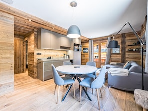 Eine moderne Küche mit Holzelementen, ein Essbereich mit rundem Tisch und Stühlen sowie eine gemütliche Sitzecke mit einer Couch und einer Lampe.