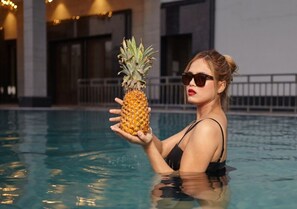 A person in a swimming pool holding a pineapple. - Palm Green Hotel and Resorts (New Delhi)