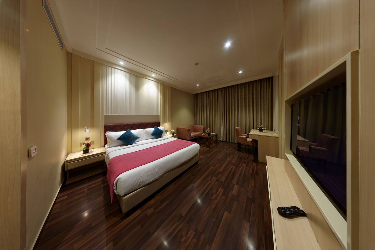 A hotel room with a large bed, a desk, a chair, a TV, and a window with curtains.