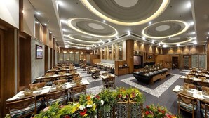 Un amplio vestíbulo de hotel con varias mesas de comedor, una zona de estar central y una pantalla grande que muestra contenido.