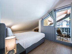 Une chambre à coucher comprenant un lit, une table de chevet, une lampe et donnant sur un balcon aménagé avec du mobilier d’extérieur.