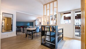 Een moderne woonkamer met een eethoek, een boekenkast en uitzicht door een glazen deur.