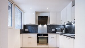 Een moderne keuken met witte kastjes, een inbouwoven, een magnetron en een raam met geëtste glas.