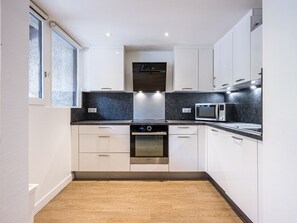 A modern kitchen with white cabinets, a built-in oven, a microwave, and a window with frosted glass.