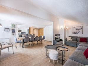 A modern living room with a grey sofa, a coffee table, and a dining area with chairs.