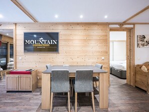 A modern interior with a wooden wall, a dining table with chairs, a bed, and a mounted sign.