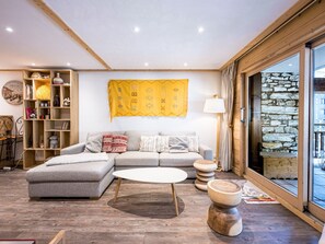 Una sala de estar acogedora con un sofá modular, una mesa de centro redonda, una estantería de madera y un ventanal con pared de piedra.