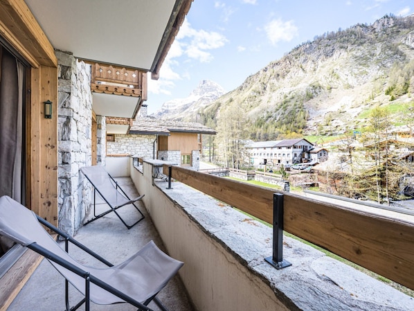 A balcony with a stone wall, wooden railing, and two chairs.