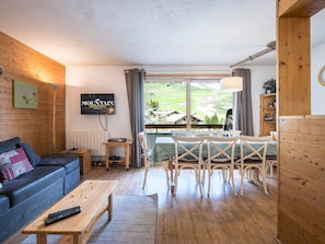 A cozy living room with a sofa, coffee table, TV, and a dining area with chairs and a table.