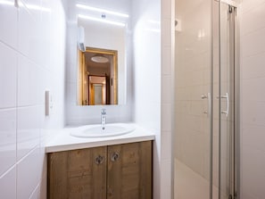 A modern bathroom with a white sink, wooden vanity, a mirror, and a glass shower enclosure.