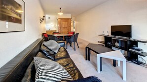 Een moderne woonkamer met een bank, een eettafel met stoelen, een tv-meubel en een keuken in de achtergrond.