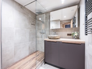 A modern bathroom with a glass-enclosed shower, a wooden vanity, and a large mirror.