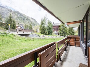 A balcony with wooden railings overlooking a grassy area with a mountain backdrop.