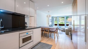 A modern kitchen with a dining area, wooden flooring, and large windows.