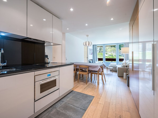 A modern kitchen with a dining area, wooden flooring, and large windows.