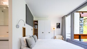 A bedroom with a large bed, a built-in wardrobe, a bedside table, and a window with a view of the outdoors.