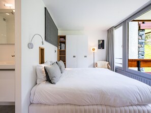 A bedroom with a large bed, a built-in wardrobe, a bedside table, and a window with a view of the outdoors.